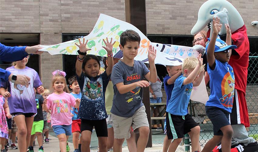 Children run through the Lab School playground reopening banner.