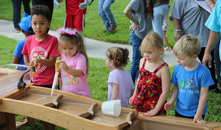 Five children play with a wooden outdoor cascade water table.